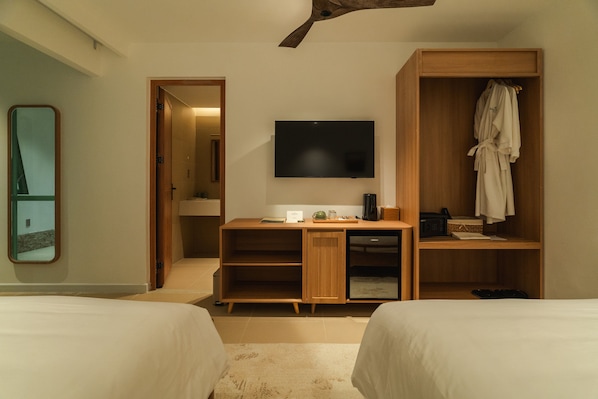 Habitación de hotel con dos camas, un escritorio, un televisor de pantalla plana, un armario y un espejo.