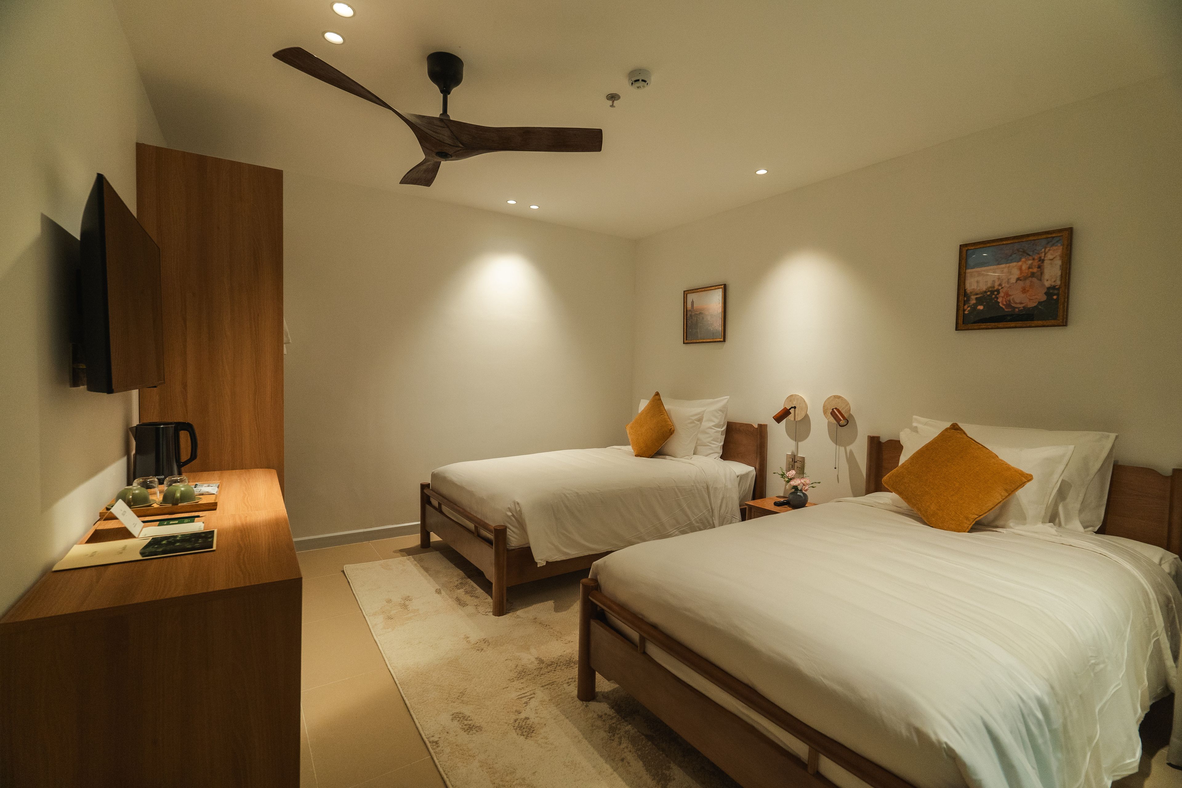 A bedroom with two beds, a ceiling fan, a coffee maker, and a painting on the wall.