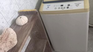 Una lavadora con panel de control, un banco de madera y una concha blanca en el suelo.