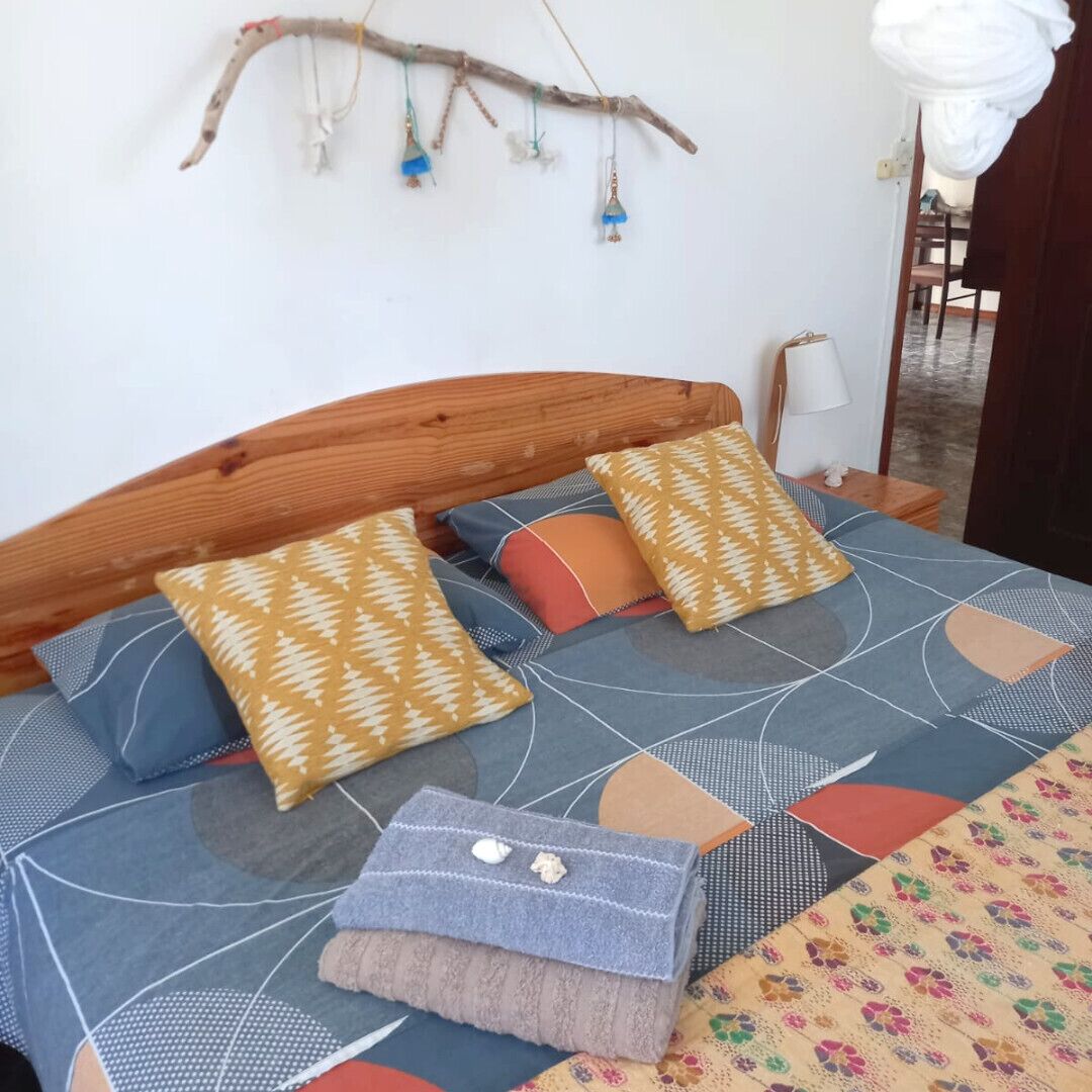 Uma cama com roupa de cama estampada, cabeceira de madeira e objetos decorativos pendurados.