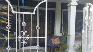 Una entrada con reja metálica decorativa, una planta en maceta y una silla de mimbre frente a un edificio con grandes ventanales.