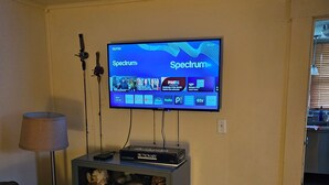 A living room with a television mounted on the wall, a small cabinet with a DVD player, a lamp, and a couch.