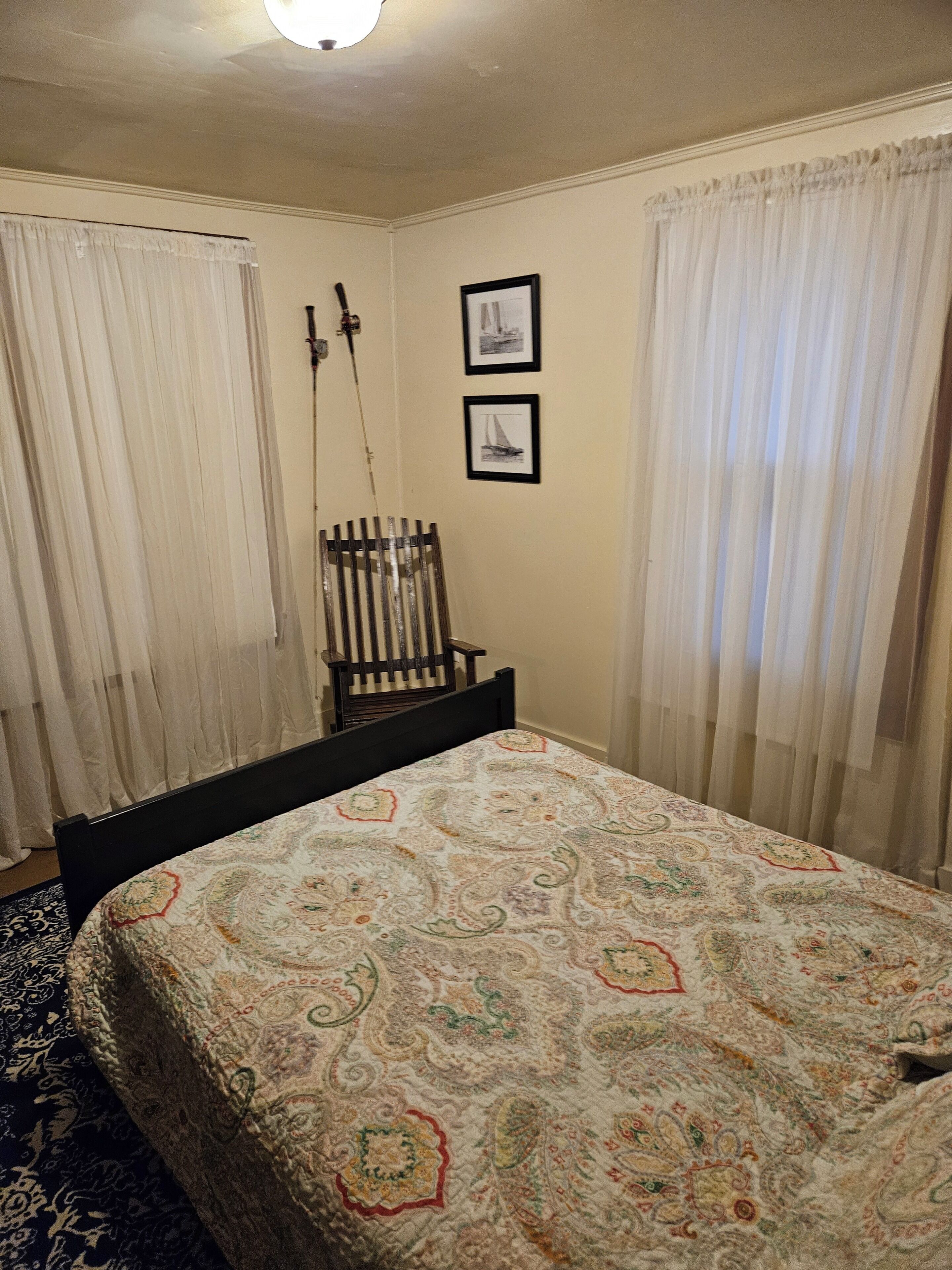 Un dormitorio con una cama, una silla y dos cuadros en la pared.