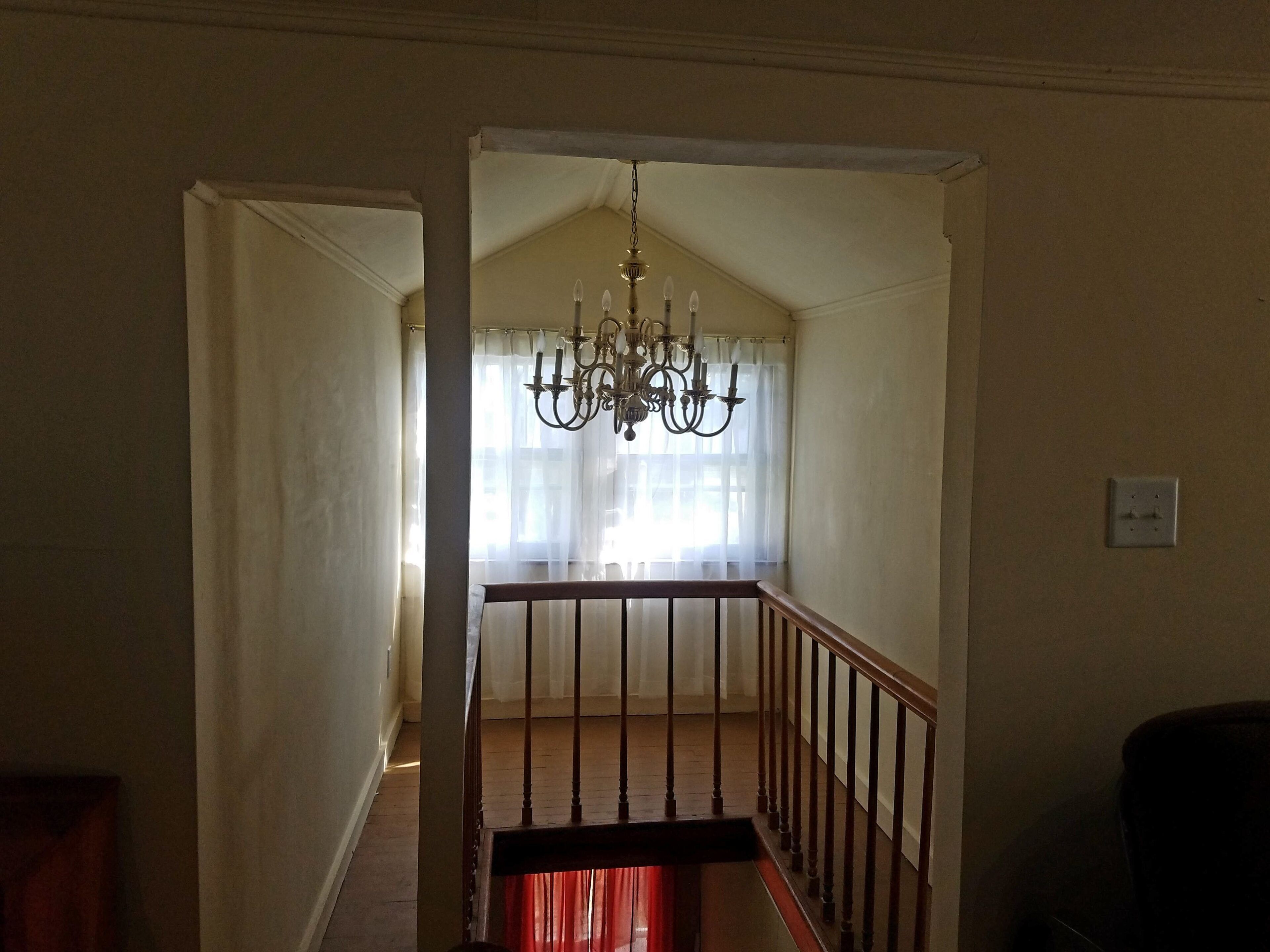 A staircase with a wooden handrail leading to a landing with a chandelier.