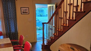 A room with a wooden staircase, a dining table with red chairs, and a patterned rug.