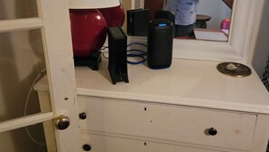 A room with a white dresser, a red lamp, and two black speakers.