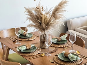 Uma mesa de jantar posta com pratos verdes, talheres dourados e um vaso decorativo com plumas de capim-dos-pampas.