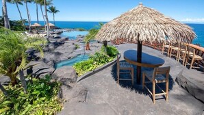 Een tropisch resort met een zwembad, rieten parasols en uitzicht op de oceaan.