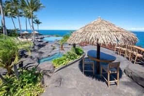 Ein tropisches Resort mit Pool, Reetdachschirmen und Blick auf den Ozean.