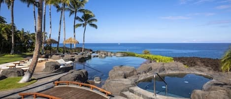 A resort with a pool, palm trees, and a view of the ocean.