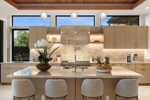 A modern kitchen with a central island, bar stools, a coffee machine, and a stone accent wall.