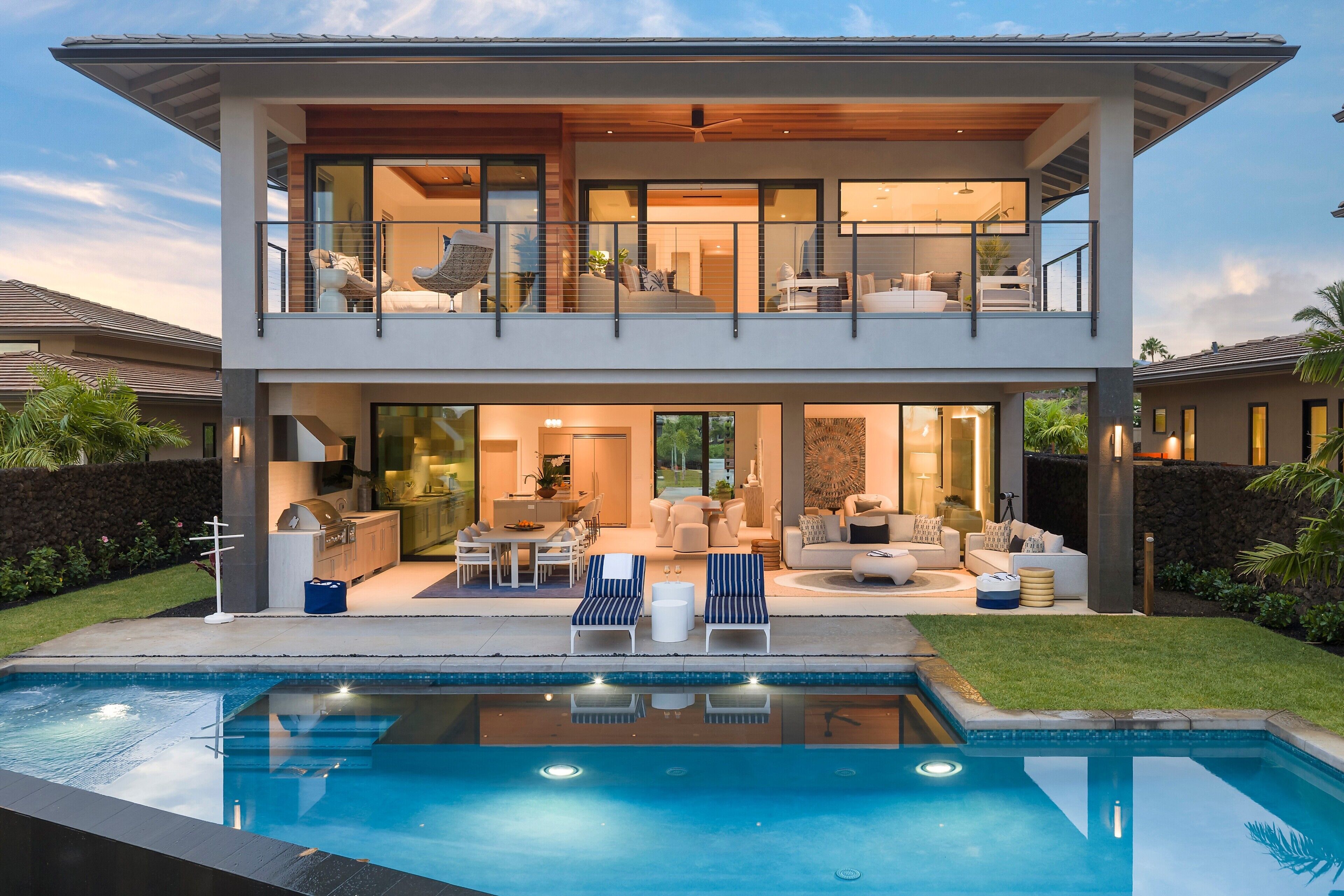 Una casa moderna de dos pisos con piscina, mobiliario de exterior e interior bien iluminado.