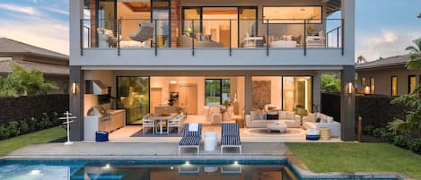 A modern two-story house with a swimming pool, outdoor seating, and a well-lit interior.