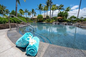 A pool with a stone border, palm trees, and a lounge chair.