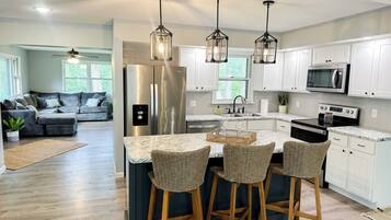 A modern kitchen with a central island, bar stools, stainless steel appliances, and pendant lighting.