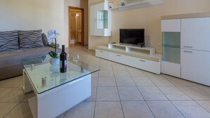 Een moderne woonkamer met een glazen salontafel, een bank, een televisie en inbouwmeubels.