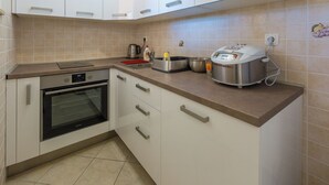 Een keuken met witte kasten, een inbouwoven, een koffiezetapparaat, een rijstkoker en een broodrooster.