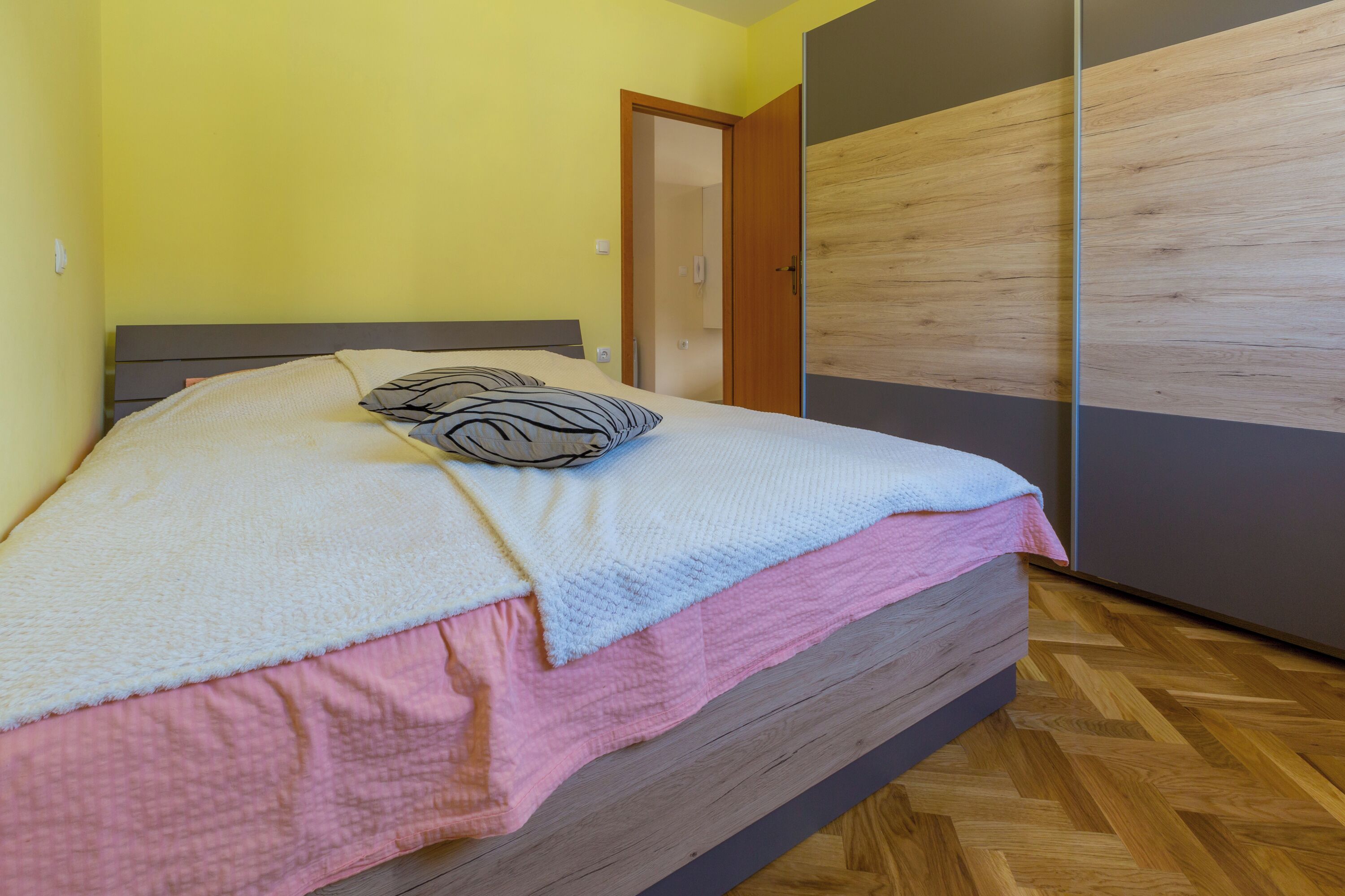 Una camera da letto con un letto, un armadio in legno e una porta che dà su un'altra stanza.