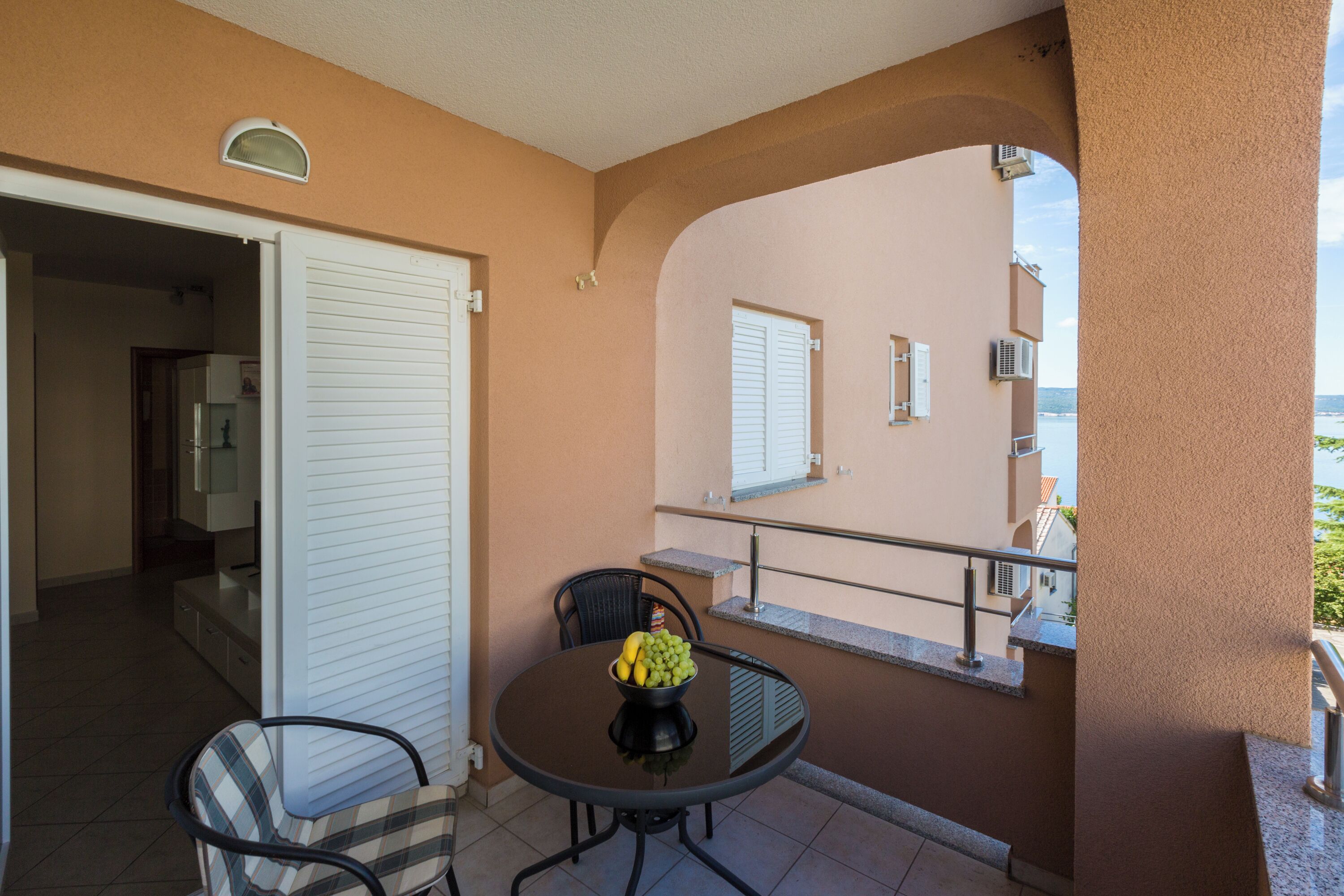 Un balcon avec une table, des chaises et un saladier rempli de fruits.