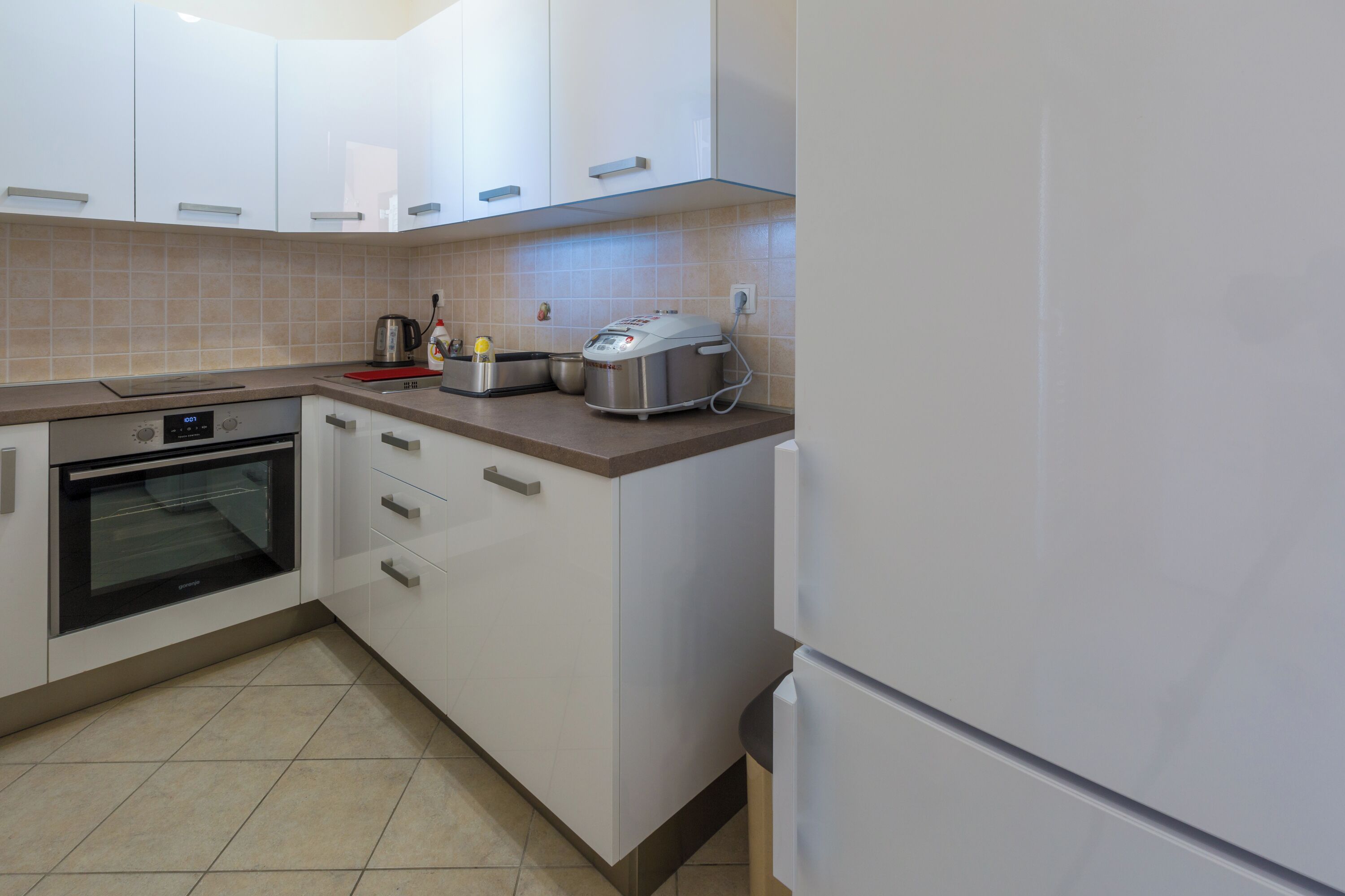 A kitchen with white cabinets, a built-in oven, a toaster, and a kettle.