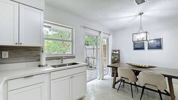 A kitchen with white cabinets, a sink, a dining table with chairs, and a chandelier.