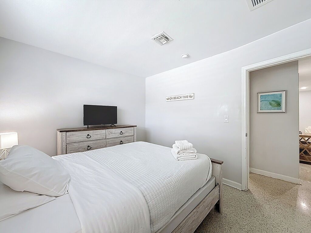 Een slaapkamer met een bed, een televisie, een dressoir en een deur naar een andere kamer.