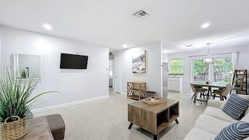 A spacious living area with a sofa, coffee table, TV, and artwork on the walls.