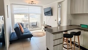 Une cuisine moderne dotée d’un îlot central, de tabourets de bar et d’un téléviseur à écran plat fixé au mur.
