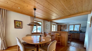 A wooden dining area with a round table and chairs, a kitchen with wooden cabinets, and a ceiling with exposed beams. - Marvelous Luxurious Furnished Flat With Outstanding Views (Rougemont)