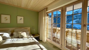 A bedroom with a large bed, a nightstand, a lamp, and a view of a snowy landscape through a sliding glass door. - Marvelous Luxurious Furnished Flat With Outstanding Views (Rougemont)