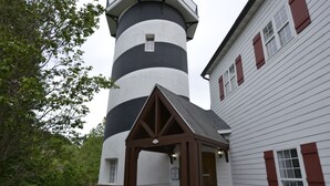 Un faro con una torre a righe bianche e nere, un padiglione in legno e un edificio bianco con persiane rosse.