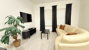 A living room with a sofa, TV, black curtains, a potted plant, and a small table. - Stylish Frisco Retreat Near The Star & Hotspots (Frisco)