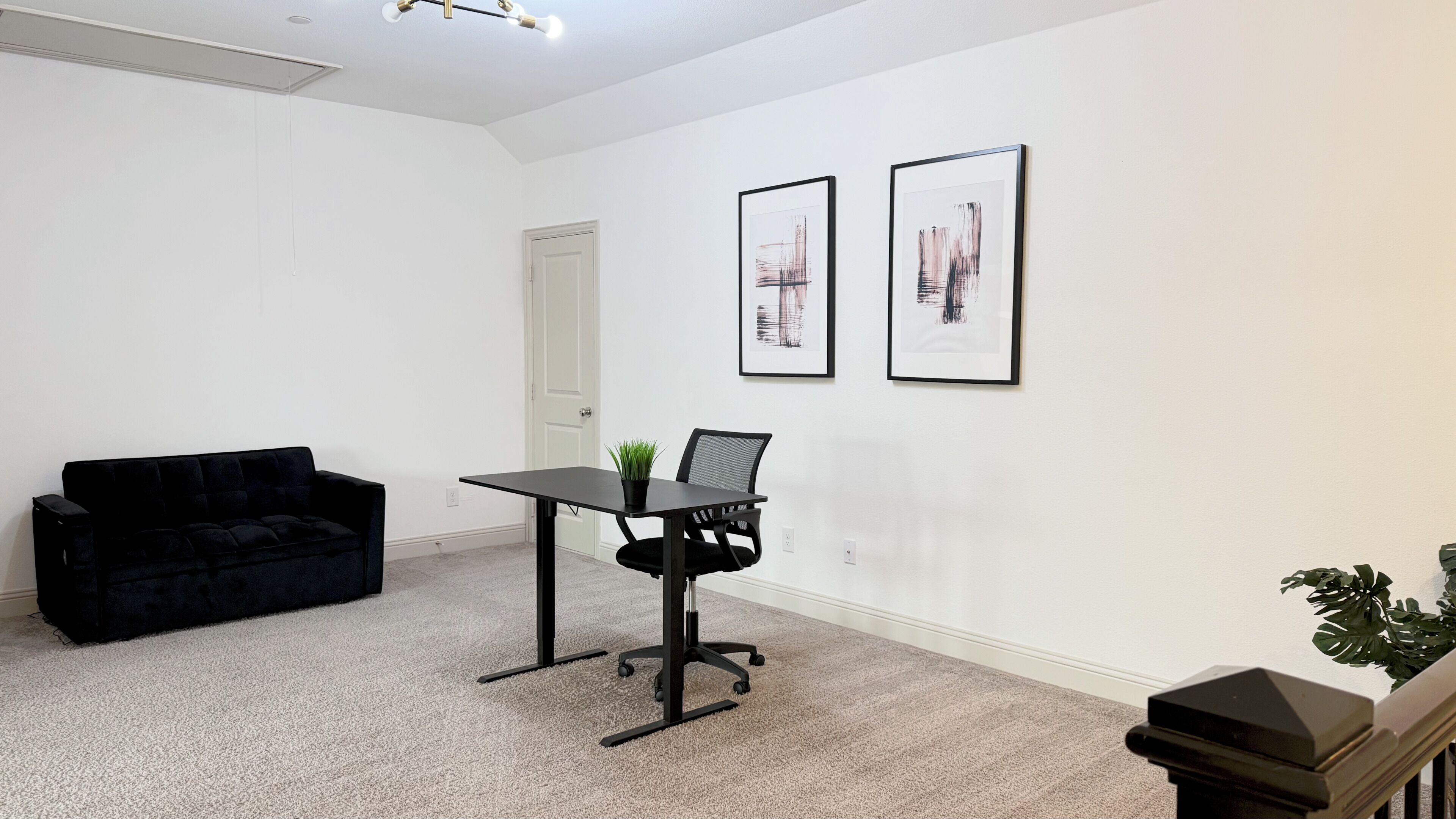 A modern room with a black sofa, a desk with a laptop, and two abstract paintings on the wall.