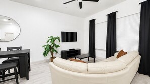 A modern living room with a sofa, a dining table, and a TV. - Stylish Frisco Retreat Near The Star & Hotspots (Frisco)