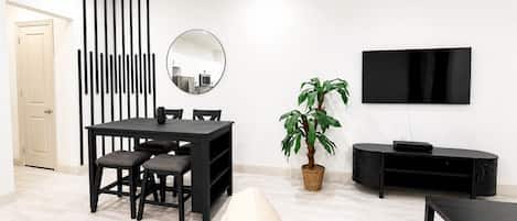 A modern living room with a dining table, chairs, a potted plant, a flat-screen TV, and a black entertainment unit.