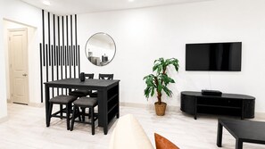 A modern living room with a dining table, chairs, a potted plant, a flat-screen TV, and a black entertainment unit. - Stylish Frisco Retreat Near The Star & Hotspots (Frisco)