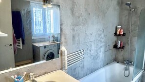 Ein Badezimmer mit Waschbecken, Spiegel, Dusche und Waschmaschine.