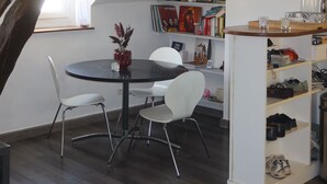 Ein Essbereich mit einem runden Tisch, weißen Stühlen, einer Hängelampe, einem Bücherregal und einem Schuhregal.