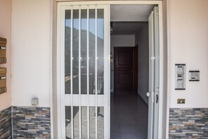 A building entrance with a sliding glass door, a stone wall, and a door leading to an interior hallway. - Mini Casa Bosa - Bosa Marina (Bosa Marina)