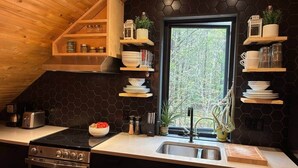 A kitchen with a stove, sink, and wooden shelves with dishes. - Chalets du plateau des Hautes-Gorges : Le Grenier (Saint-Aimé-des-Lacs)