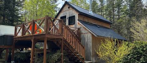 A rustic cabin with a wooden deck and stairs leading to a metal roof.