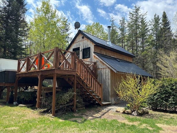 A rustic cabin with a wooden deck and stairs leading to a metal roof.