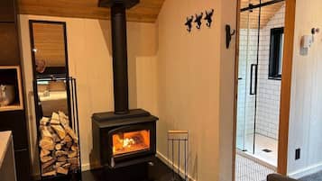 A room with a wood-burning stove, a glass door leading to a shower area, and a stack of firewood.