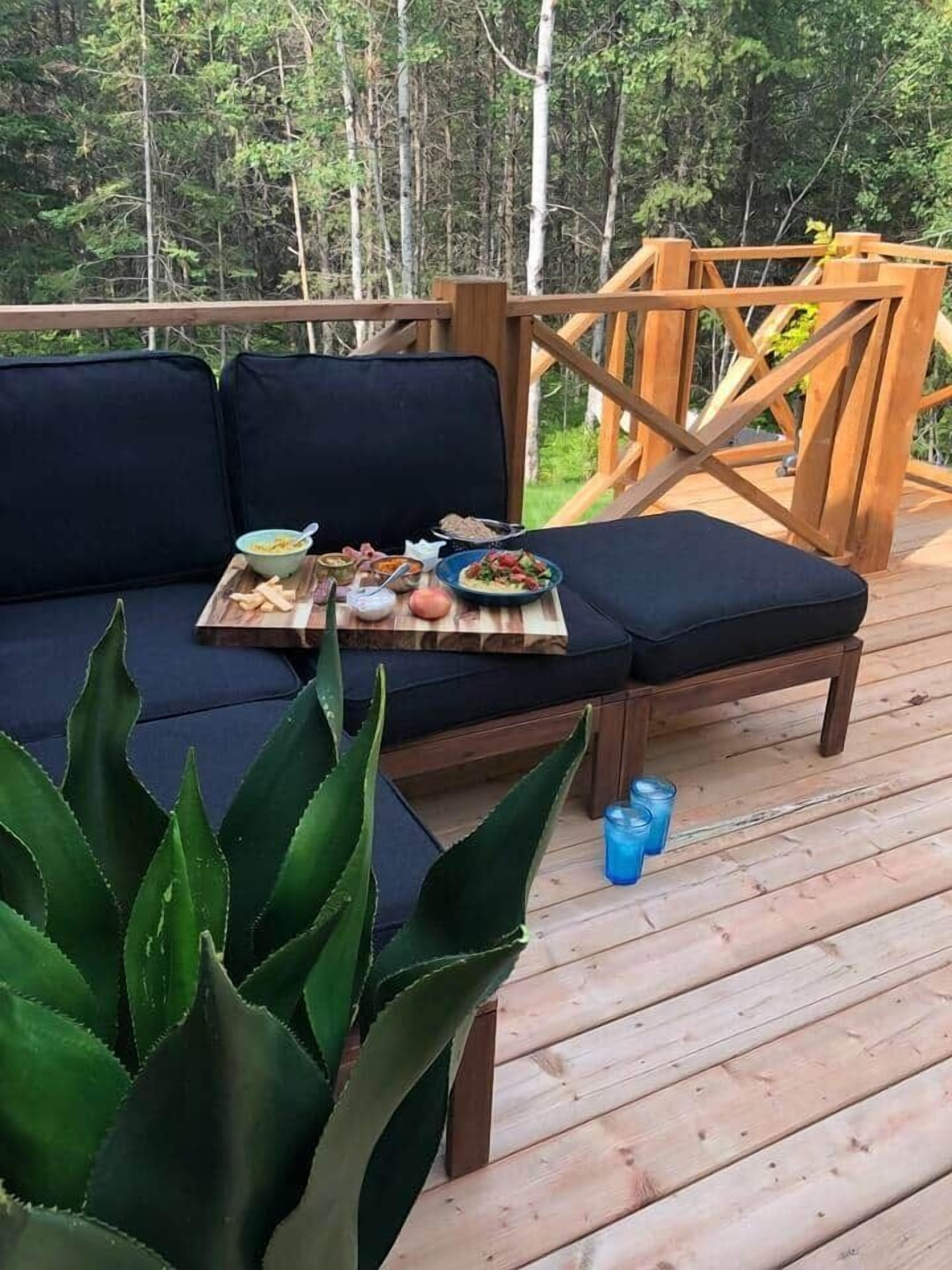 Une terrasse en bois avec un canapé et une petite table d’appoint sur laquelle sont disposés de la nourriture et des boissons.