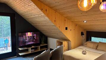 A cozy room with a TV, a bed, and a window overlooking a deck.