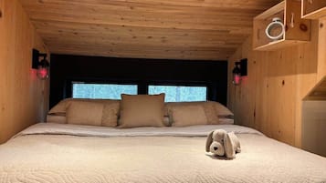 A wooden-paneled room with a bed, pillows, a stuffed toy, and wall-mounted lights.