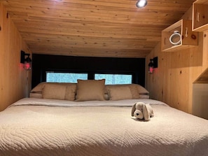 Ein Zimmer mit Holzwänden, einem Bett, Kissen und einer Wandleuchte, inklusive Stofftiers.