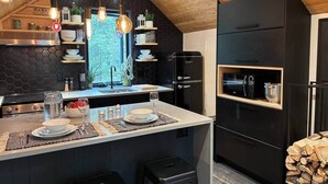 A modern kitchen with a central island, black cabinetry, and a wooden ceiling. - Chalets du plateau des Hautes-Gorges : Le Grenier (Saint-Aimé-des-Lacs)