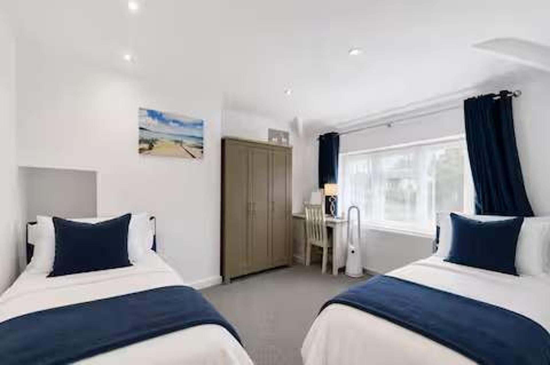 Une chambre d’hôtel avec deux lits, un bureau, une chaise, une fenêtre avec des rideaux et une porte.