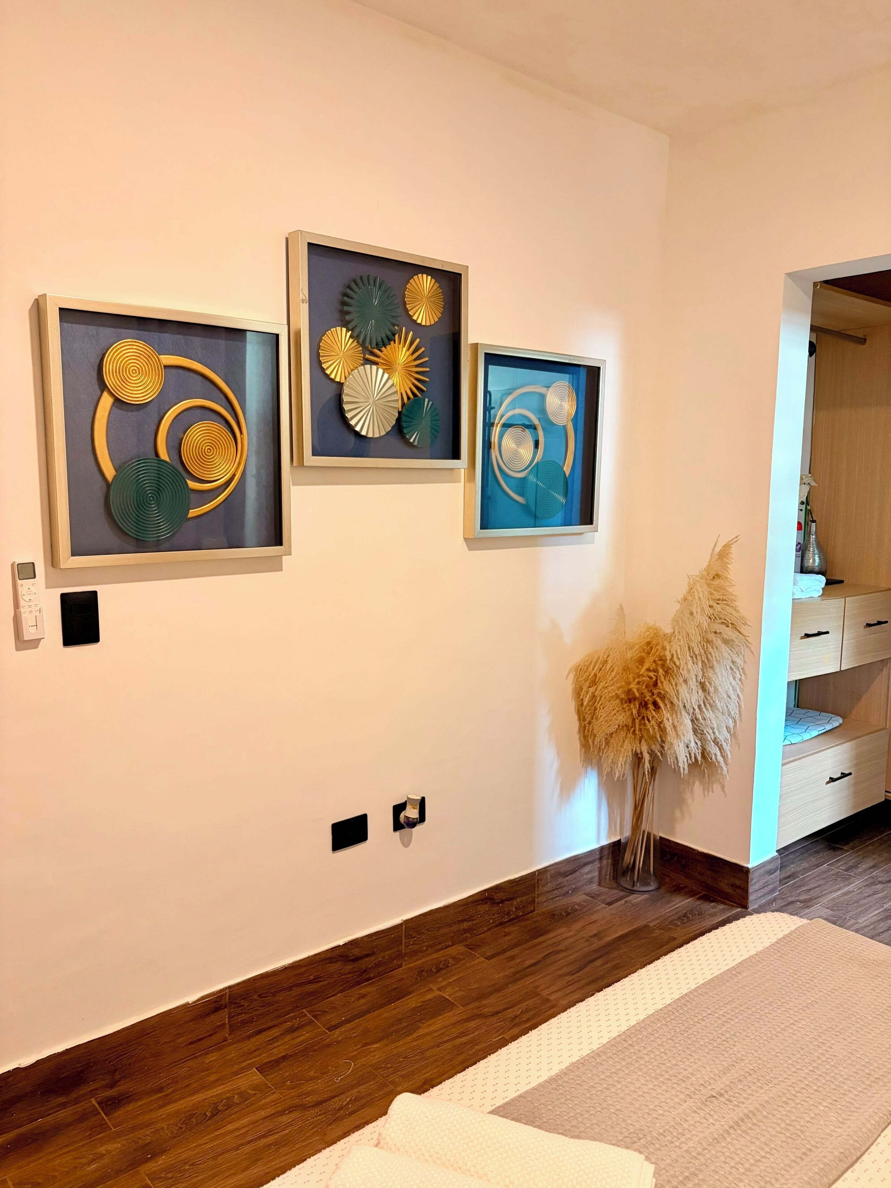 Una habitación con tres cuadros enmarcados, piso de madera, alfombra blanca y un mueble de madera.
